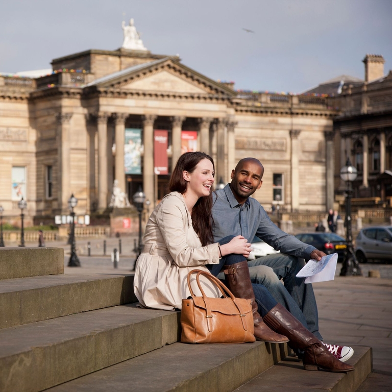 Liverpool city centre. Lime Street. Two people, a couple, sitting on the steps outside St George's Hall in front of the Walker Art Gallery, in Liverpool.
