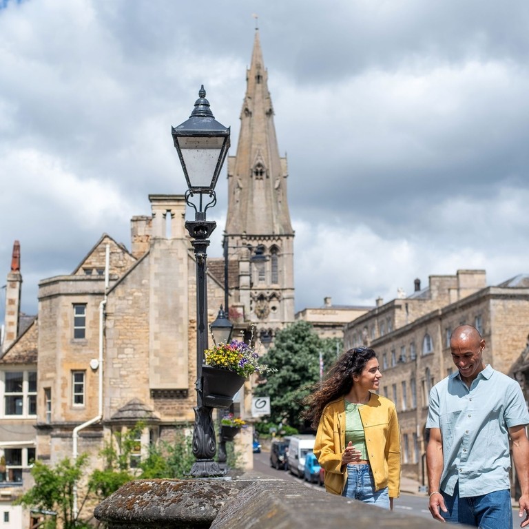 A man and a woman walk through a stone built village with a church
