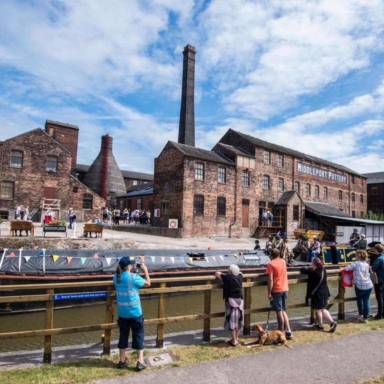 A group of people looking across the Trent and Mersey Canal at several historic buildings in Stoke