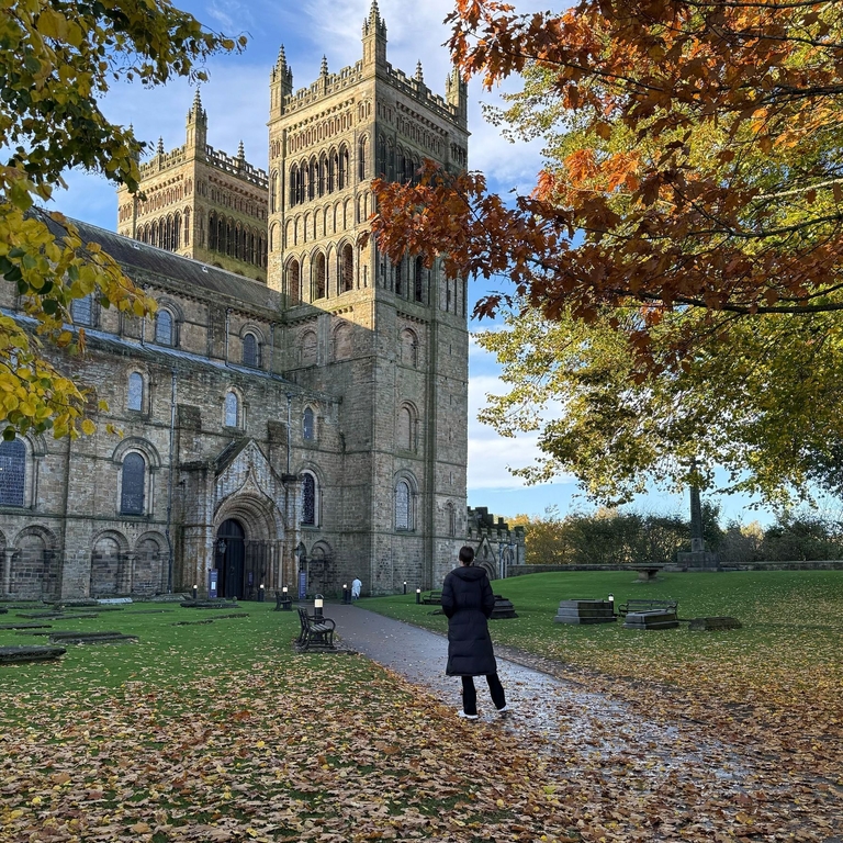 A woman in a warm jacket facing a large cathedral and tower.