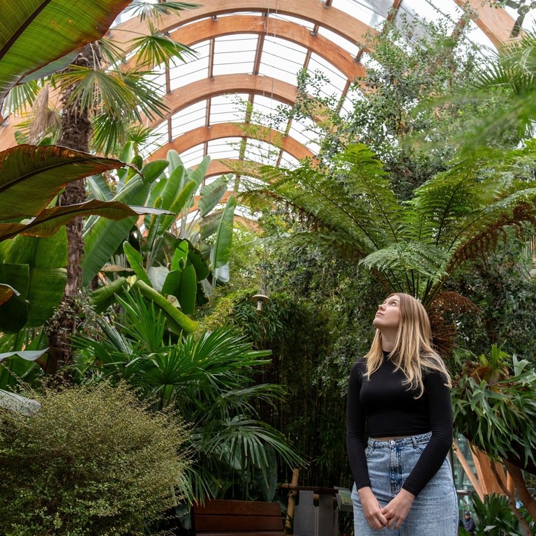 A woman walking past plants in a large temperate glasshouse