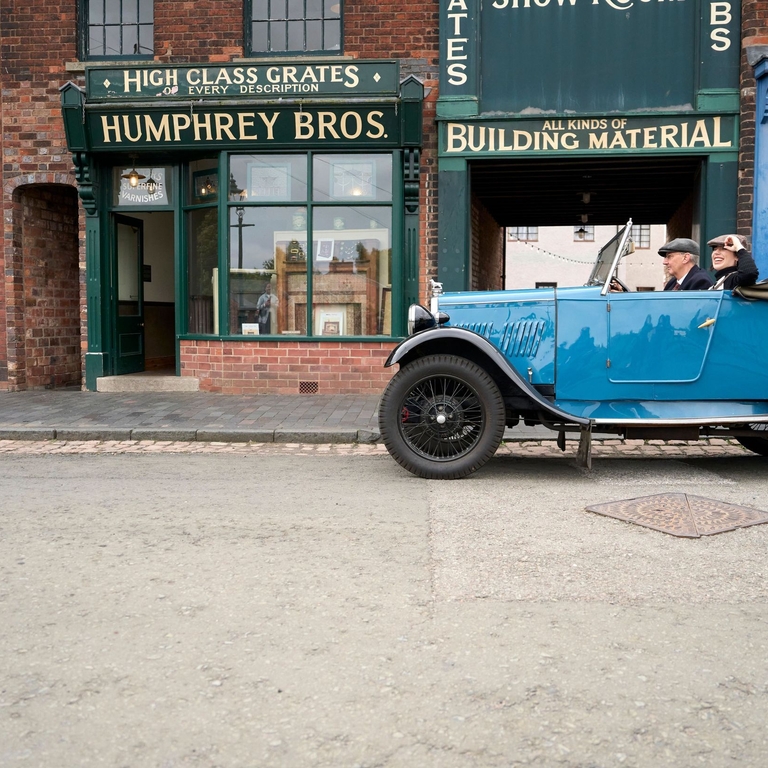 Two people inside a vintage car at a living museum