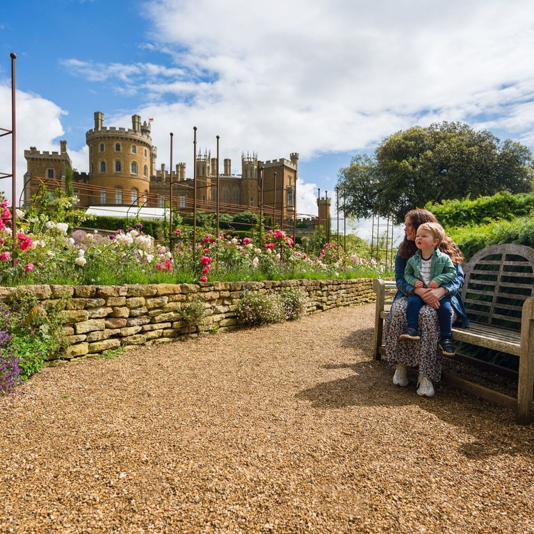 A woman sits on a bench with her child on her lap in front of a castle 
