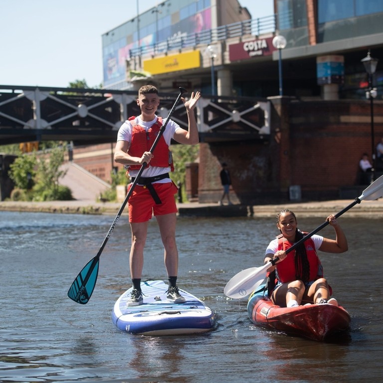 Two men kayaking on canal through central Birmingham