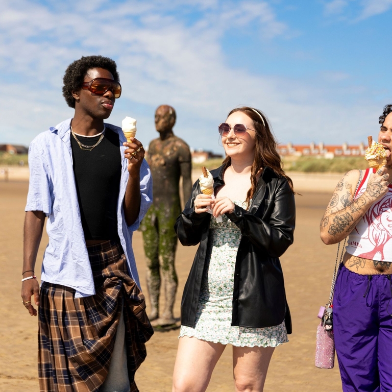 A group of friends walk on the beach with ice creams, a statue in the background