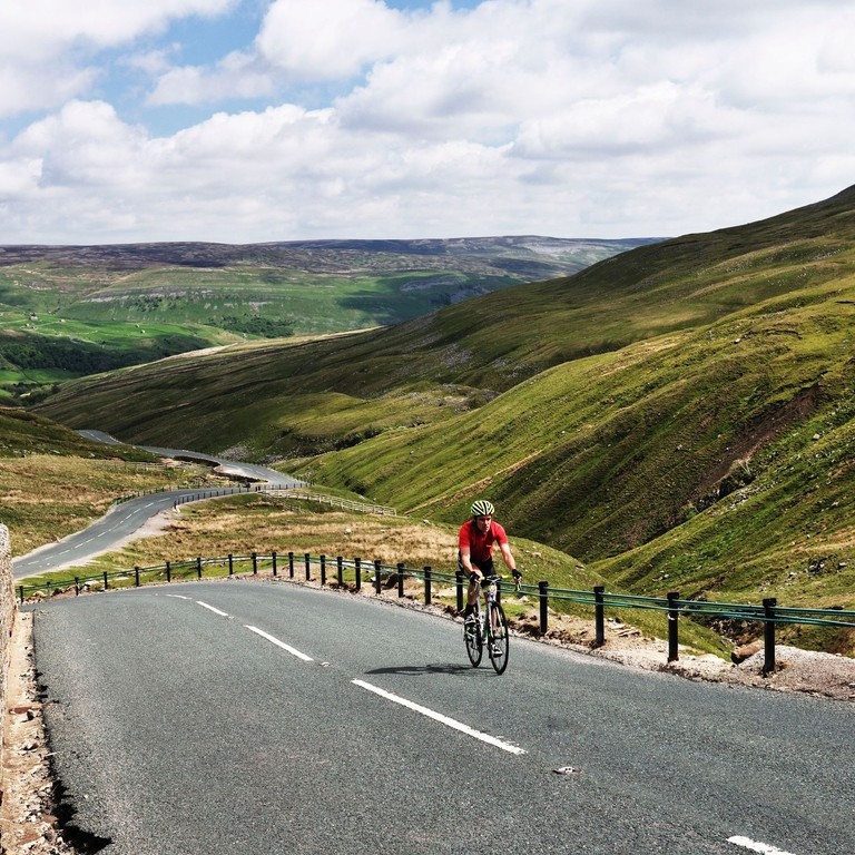 Cyclist riding on road through green dales