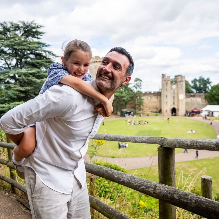 A man holds his daughter on his back in front of a heritage castle