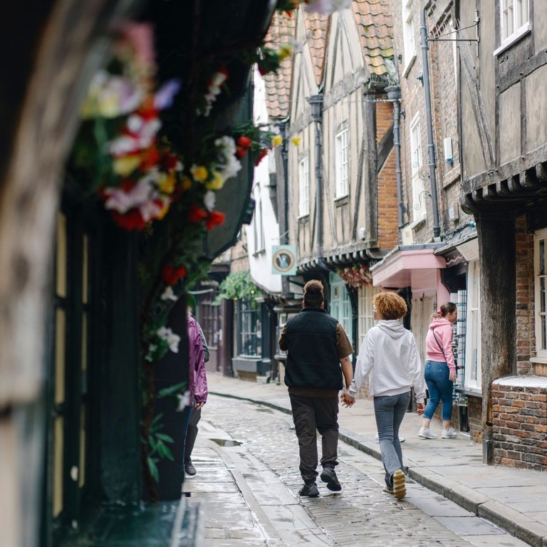 A man and a woman walk down a cobbled street holding hands