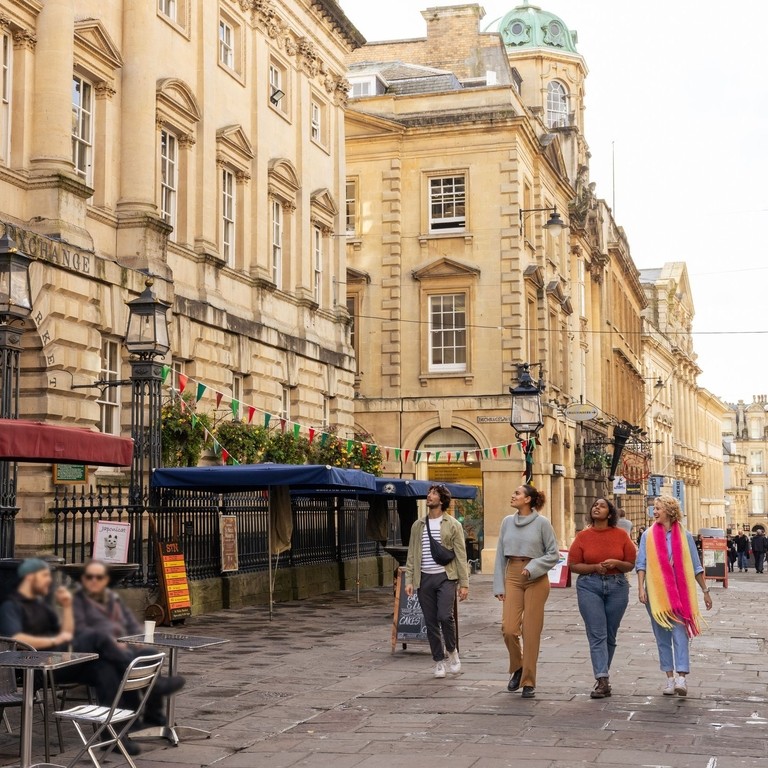 Friends walking in front of old historic buildings, on a cobbled street.