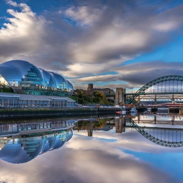 A modern glass international music centre along a calm river next to an arched bridge.