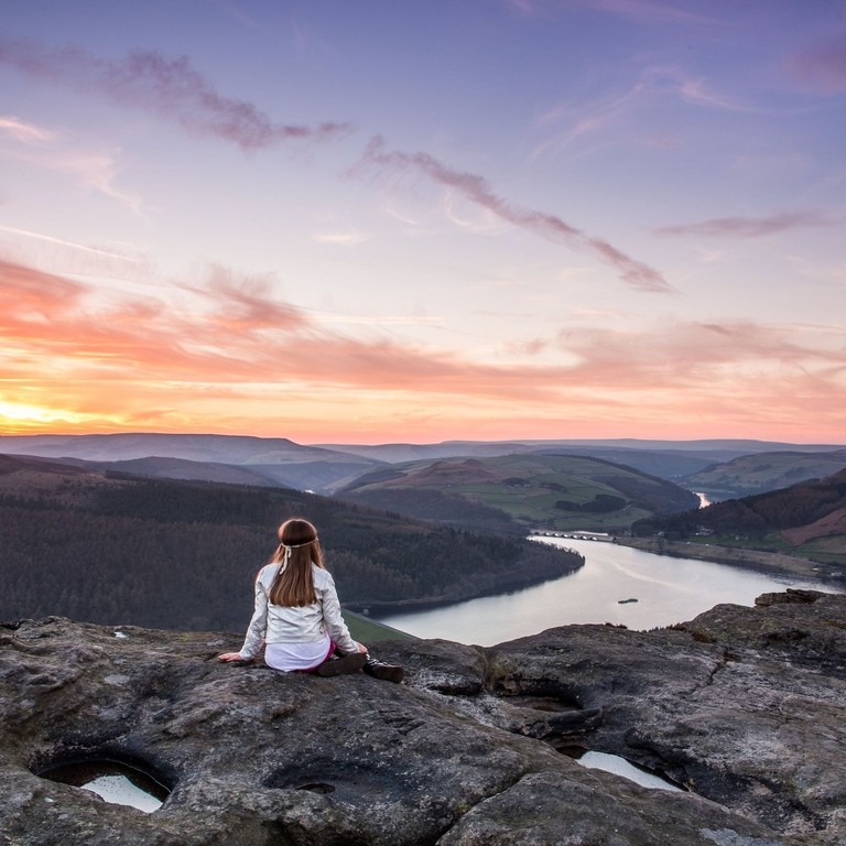 A woman sitting on rocks looking down valley to the river