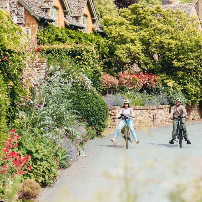 A man and and woman cycle through a quaint village