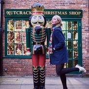 Woman posing beside a nutcracker prince statue, outside a christmas shop